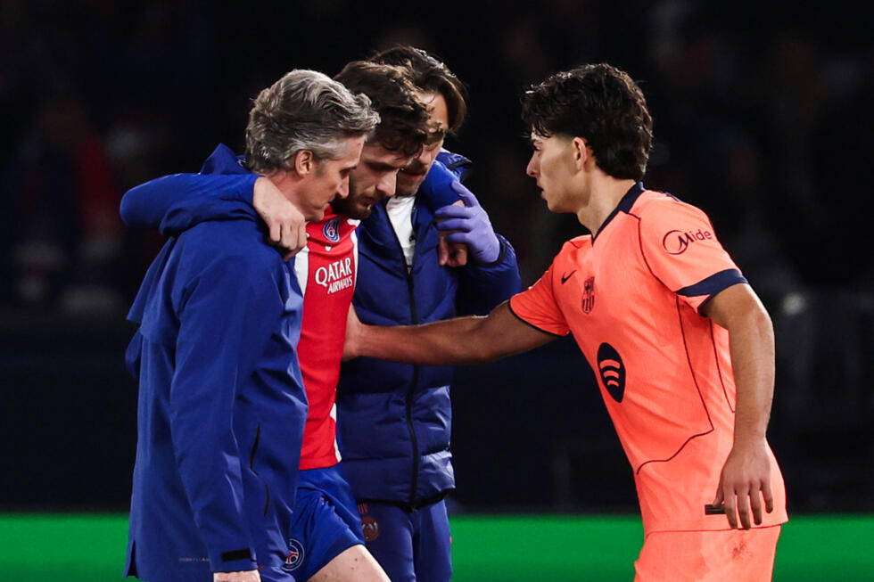 Khvicha Kvaratskhelia, del PSG, es ayudado a salir del campo tras lesionarse en una acción con Xavi Espart (derecha), del Barcelona, en la victoria del equipo francés en un partido de la Liga de Campeones. En París, el 20 de octubre de 2026 © FRANCK FIFE / AFP